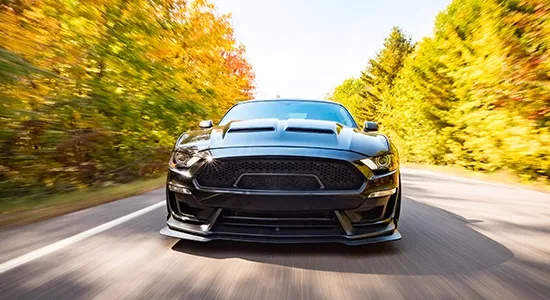 A black Mustang cruises a country road in the fall.